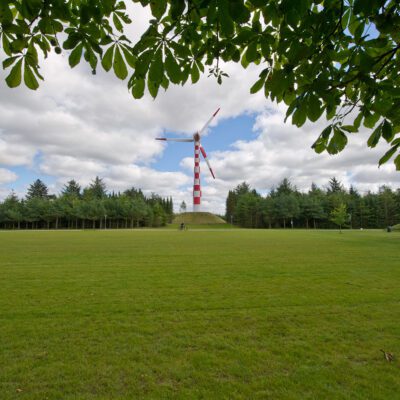 Tvindkraft wind turbine with green lawn and horse chestnut foliage in the foreground