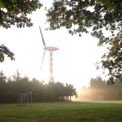 Sunrise behind the Tvindkraft wind turbine with trees and leaves.